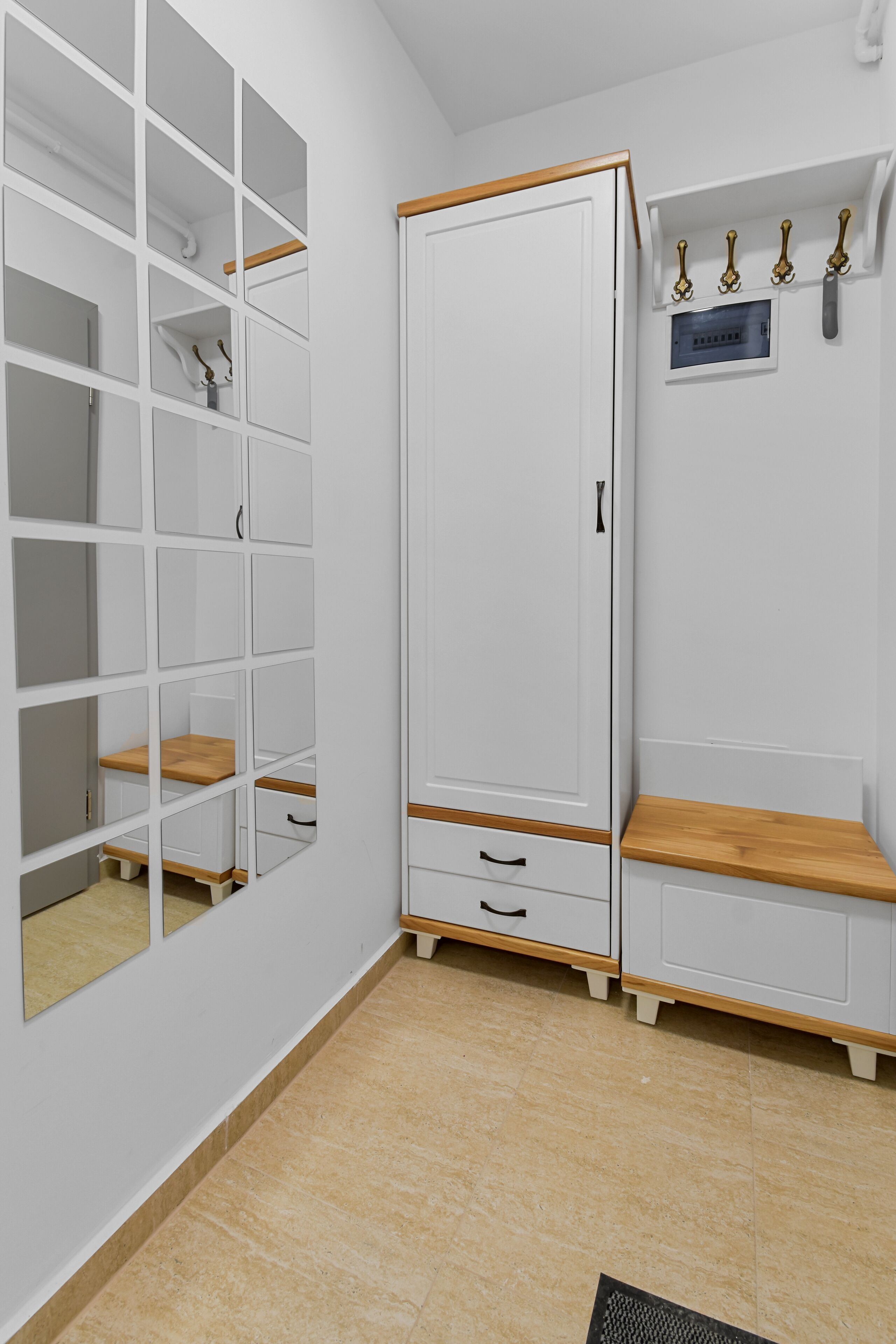 Un armario blanco con varios compartimentos, un banco de madera y un perchero con ganchos.