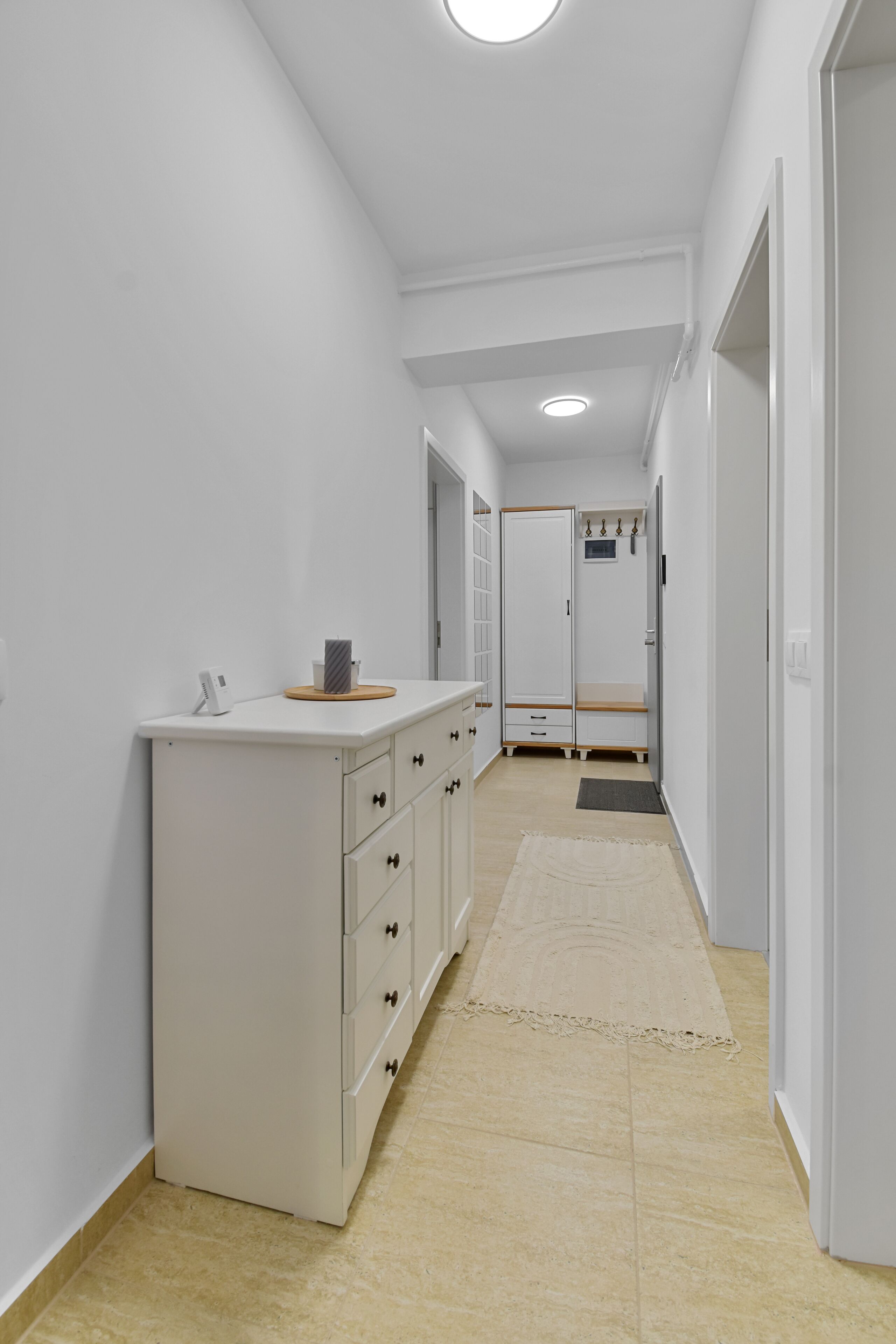 A narrow hallway with a white cabinet, a small rug, and a door leading to a room.