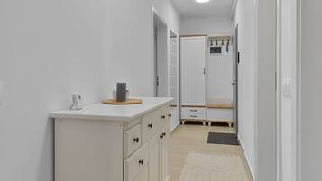 A narrow hallway with a white cabinet, a small rug, and a door leading to a room.