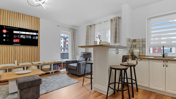 A modern kitchen with a wooden countertop, two bar stools, a grey sofa, and a flat-screen TV mounted on the wall. - Karina 2BDR Apartment (Brasov)