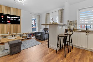 A modern kitchen with a wooden countertop, two bar stools, a grey sofa, and a flat-screen TV mounted on the wall. - Karina 2BDR Apartment (Brasov)