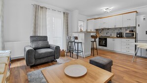 A modern living room with a grey sofa, a wooden coffee table, and a kitchen area with white cabinets and a microwave. - Karina 2BDR Apartment (Brasov)