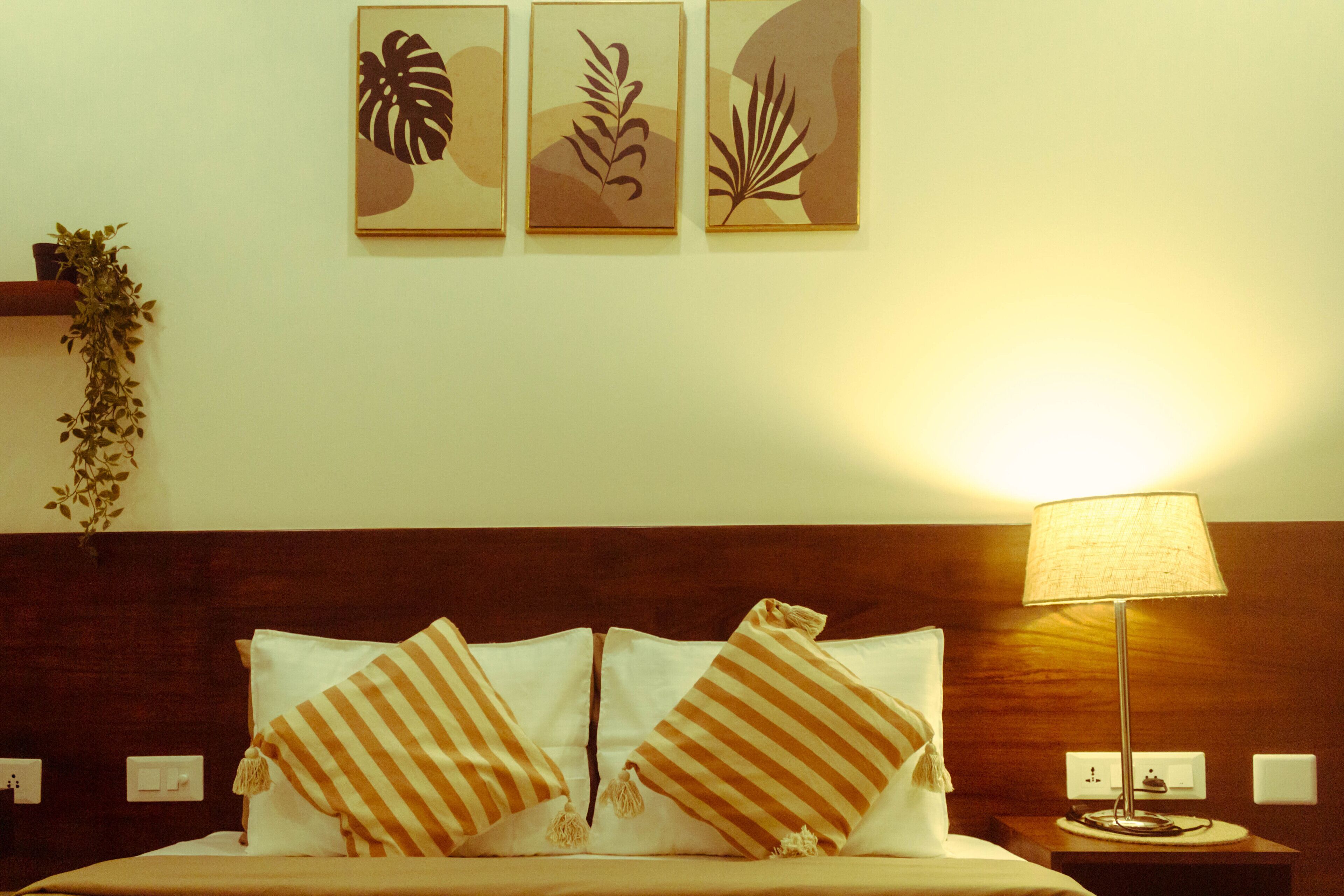 Una habitación de hotel con una cama, almohadas a rayas, una mesita de noche con una lámpara y decoración en la pared.