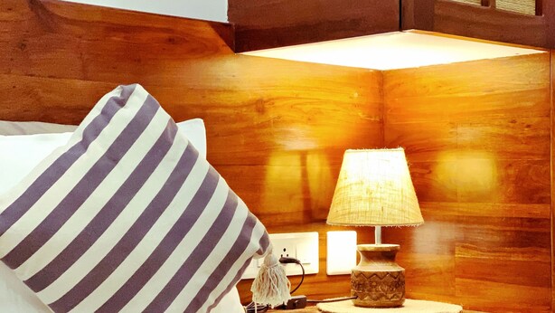 A neatly made bed with a striped pillow, a bedside lamp, and a small decorative item on the nightstand. - Casa Mel (Puducherry)