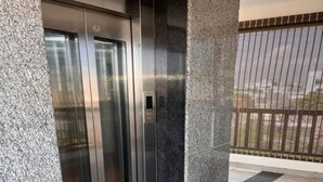 An elevator with a metallic finish, adjacent to a textured stone wall and a tiled floor. - Casa Mel (Puducherry)