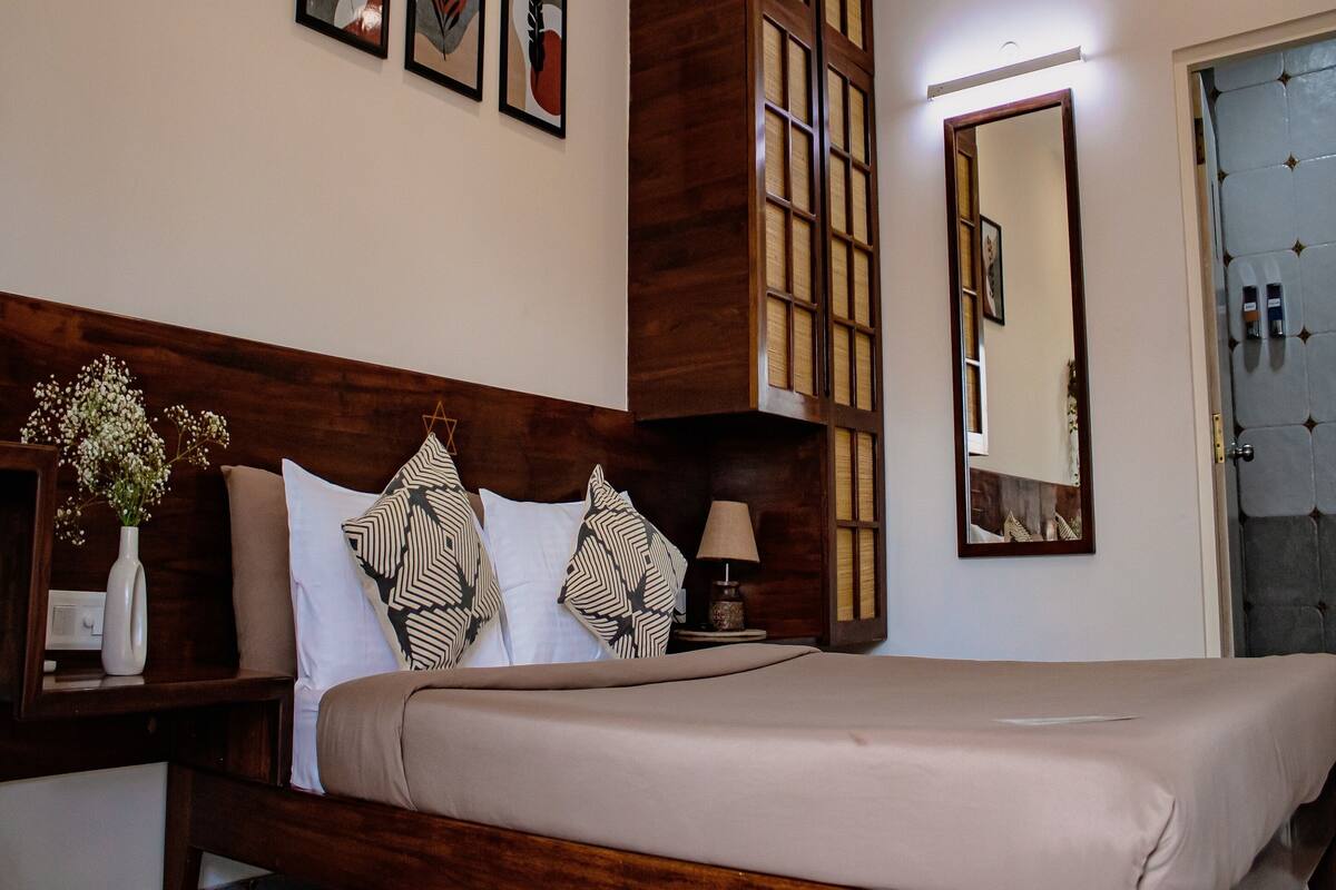 Habitación de hotel ordenada con cama, mesita de noche, espejo y cuadros en la pared.