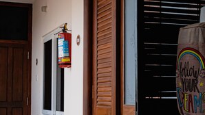 A hallway with a wooden door, a fire extinguisher, and a bench. - Casa Mel (Puducherry)