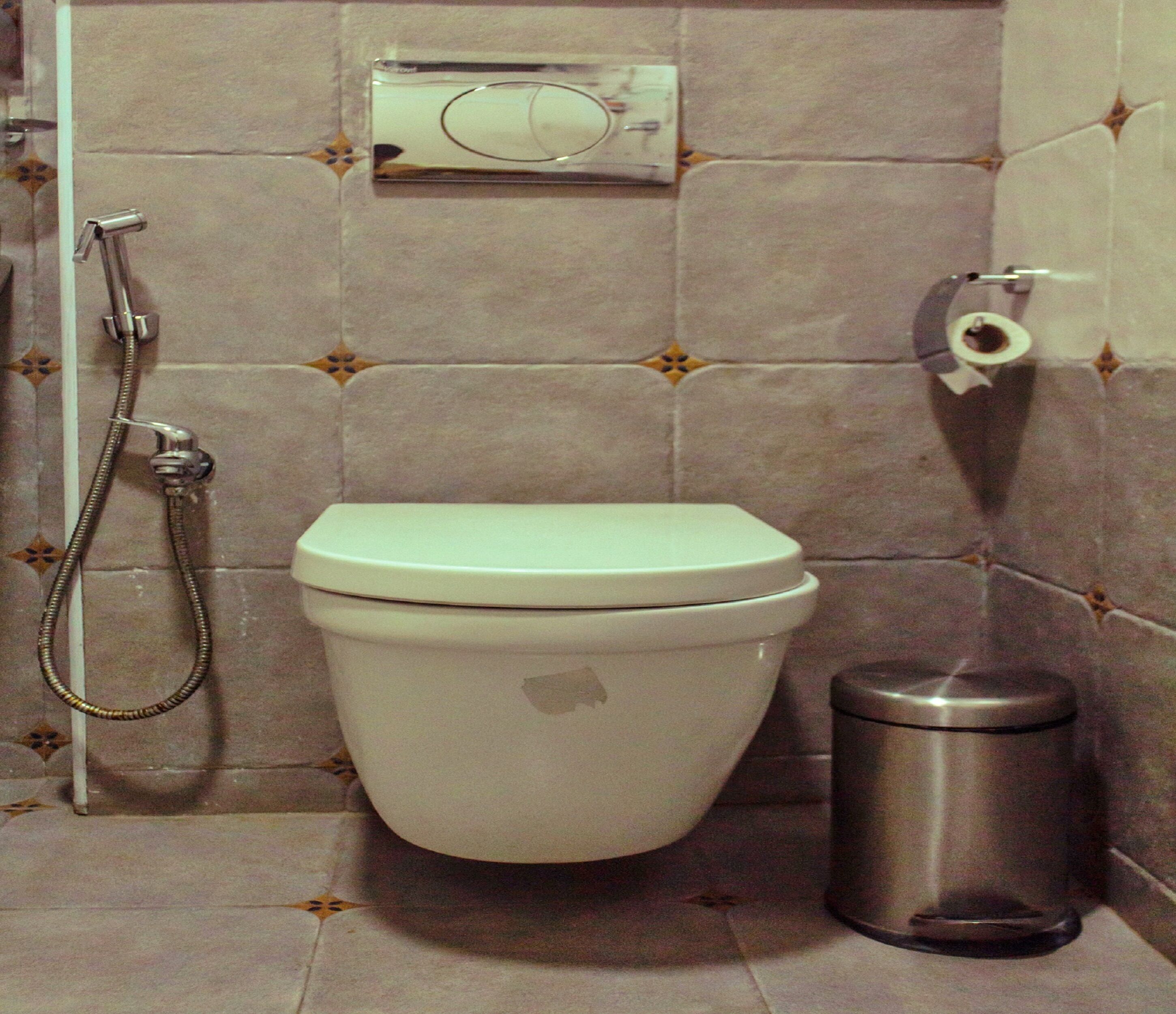 A bathroom with a toilet, a shower, and a trash bin.
