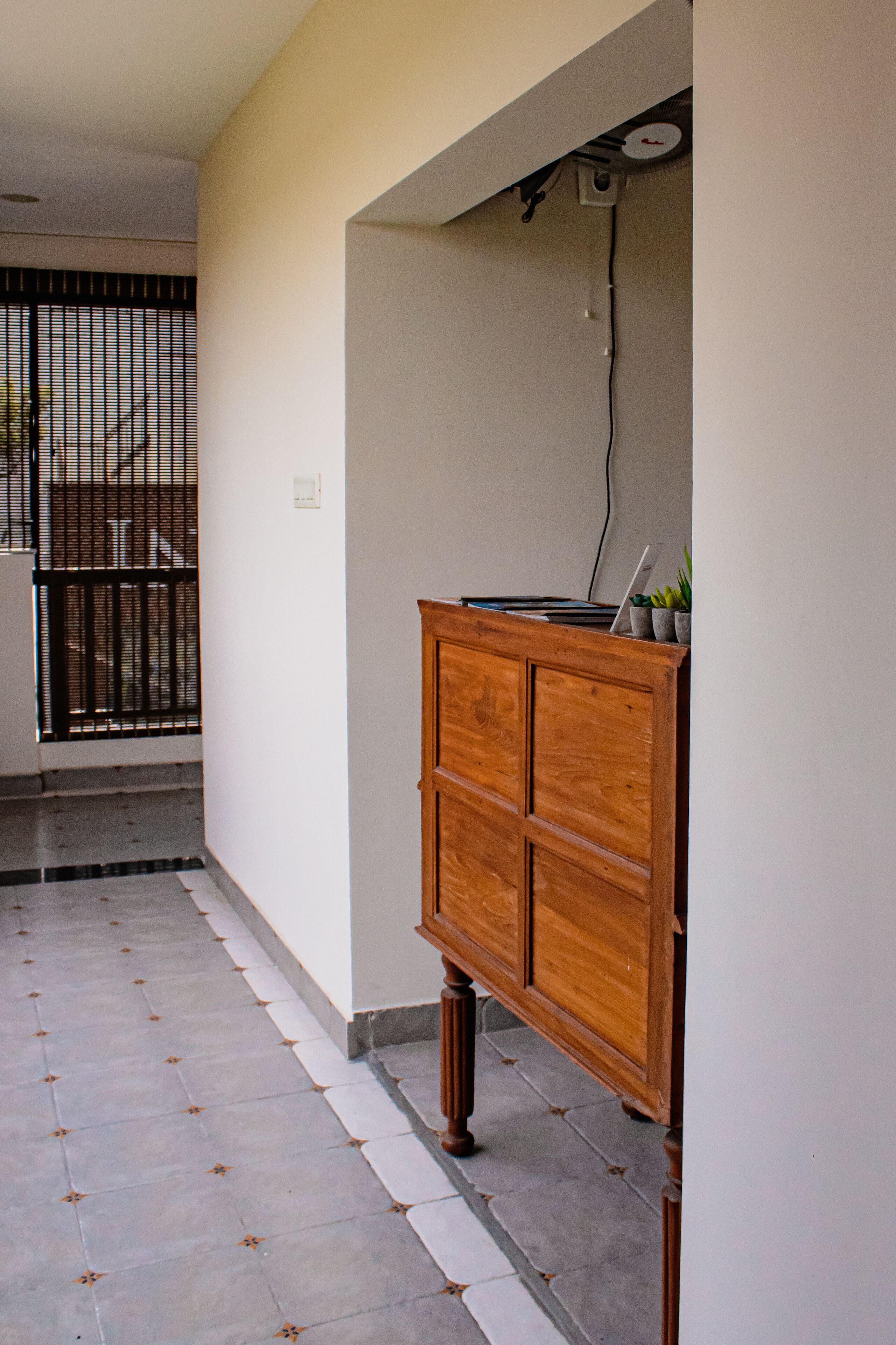 A hallway with a wooden cabinet, a tiled floor, and a gate in the background.