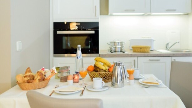 Colazione servita con pane, frutta e bevande su un tavolo in una cucina moderna.