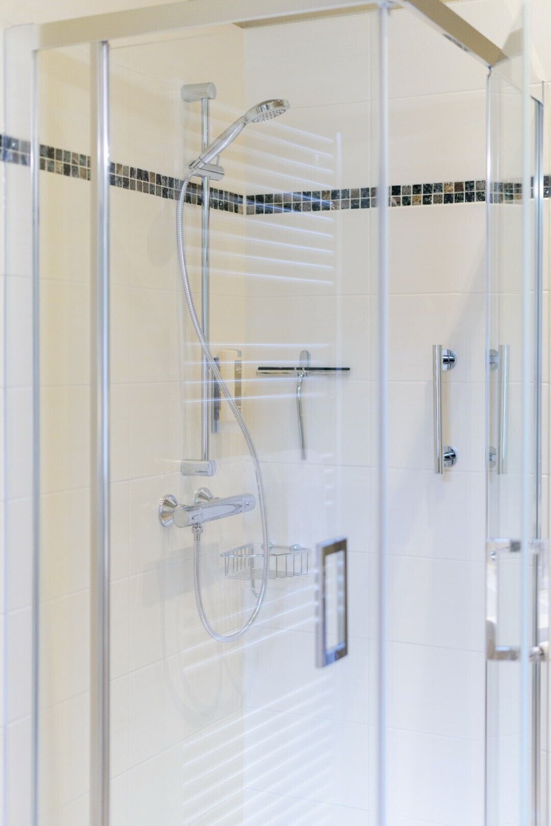 A glass-enclosed shower with a handheld showerhead, a wall-mounted faucet, and a control panel.