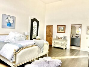 A bedroom with a bed, dresser, and a door leading to another room.