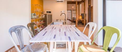 A dining area with a long table, chairs, and a kitchen in the background.