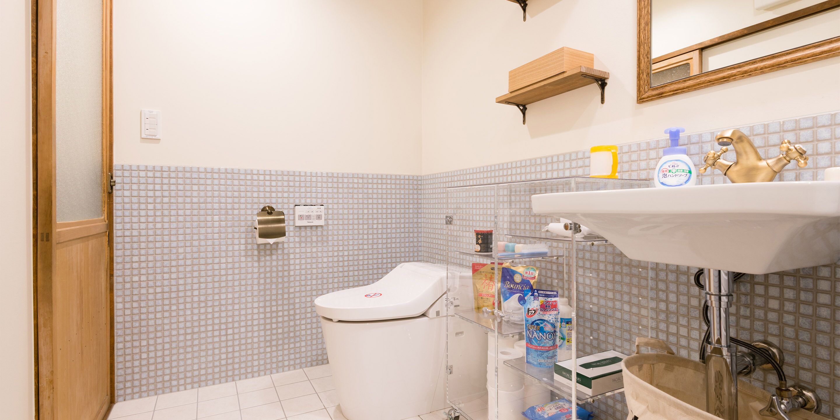 A bathroom with a toilet, sink, and shelves with toiletries.