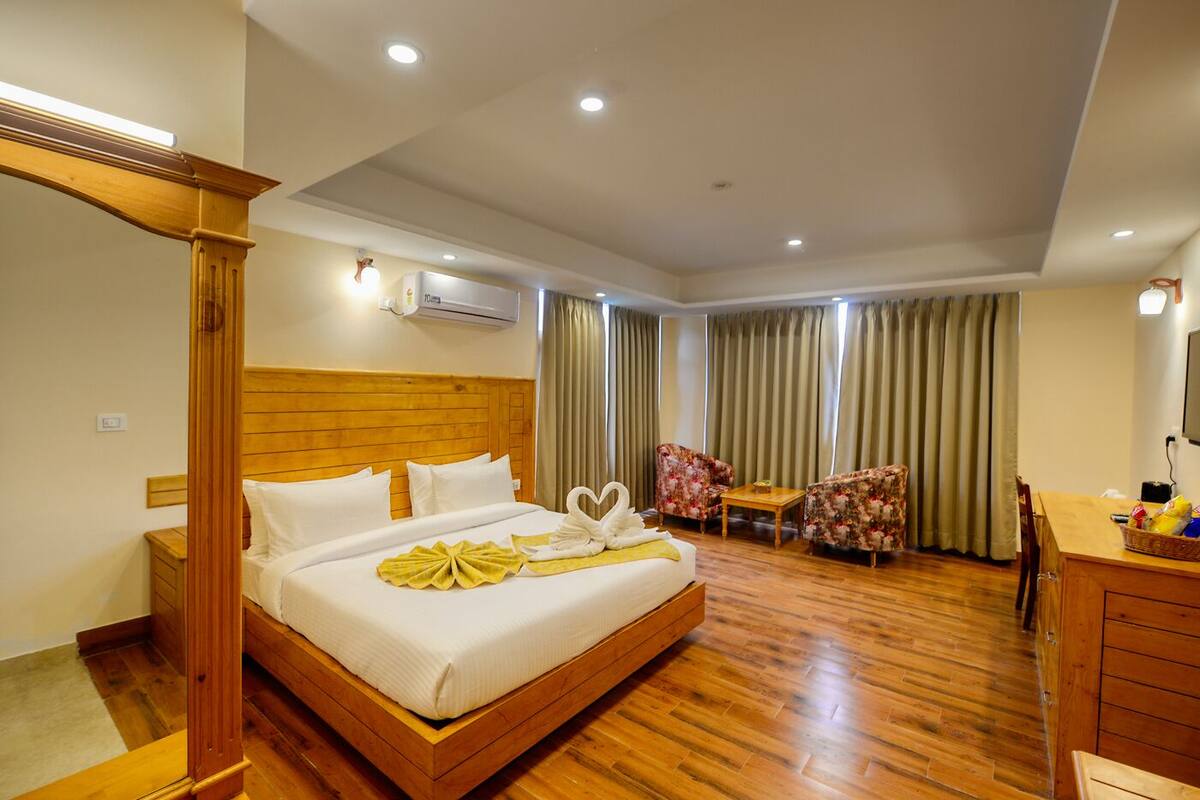 A hotel room with a wooden bed, a wooden nightstand, a desk with a chair, a small table, and a TV.