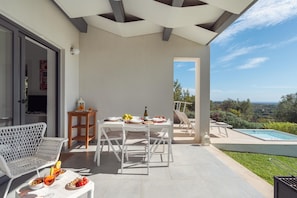 A patio with a dining table set for two, a pool, and a view of the landscape.