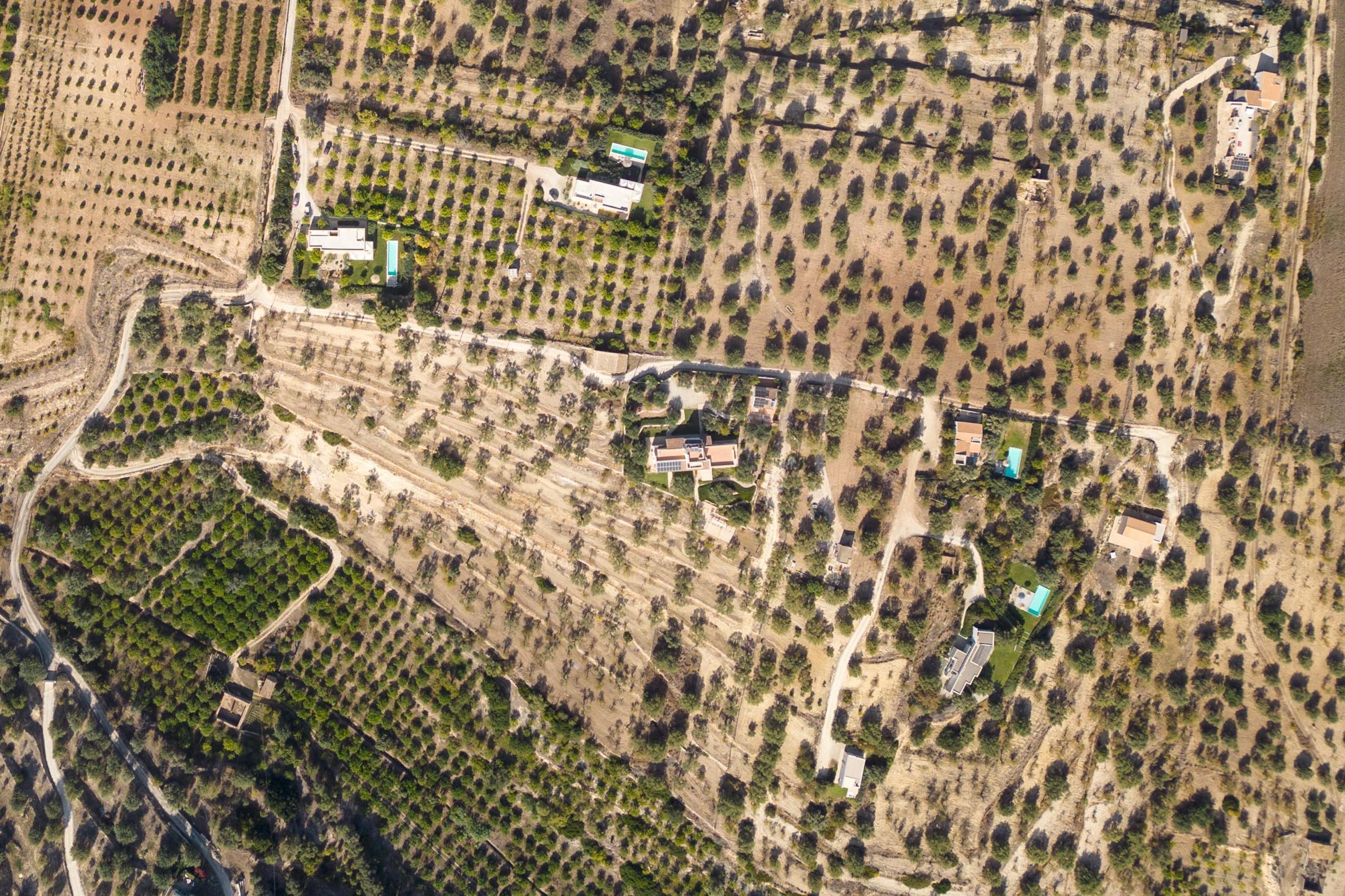 An aerial view of a property with multiple buildings, including a large house with a swimming pool, surrounded by landscaped gardens and fields.