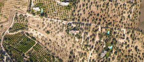 An aerial view of a property with multiple buildings, including a large house with a swimming pool, surrounded by landscaped gardens and fields.