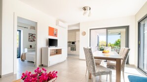 A modern living room with a dining area, a TV, and a kitchen in the background. - Villa Papeda in Noto (Noto)