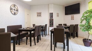 Een restaurant met meerdere tafels en zitjes, een klok aan de muur, en een aan de muur bevestigde televisie.