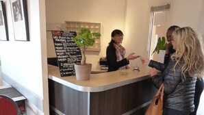 Een receptiegedeelte met een houten receptiebalie, een prikbordmenu en een kamerplant.