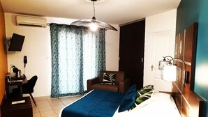 Une chambre d’hôtel avec un lit, un bureau, une chaise, une télévision et une fenêtre avec des rideaux.