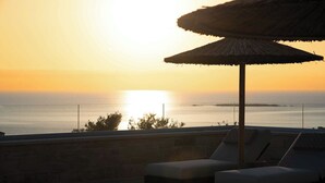 A sunset view from a balcony with lounge chairs and a thatched umbrella.