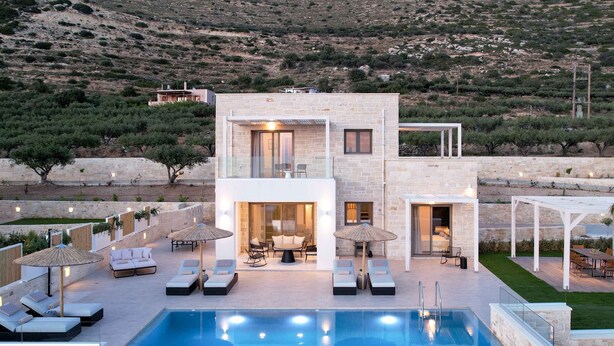 A modern two-story building with a swimming pool, outdoor seating, and a view of a hilly landscape.
