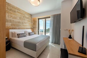 Un dormitorio con pared de piedra, una cama con ropa de cama blanca, un escritorio de madera y un televisor.