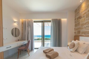 A bedroom with a bed, a desk, a chair, and a view of the ocean.