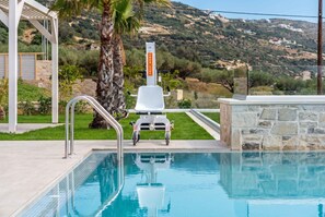 Una piscina con una silla y un puesto de socorristas, rodeada de vegetación y un paisaje montañoso.