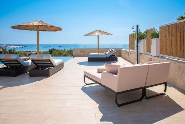 Terraza en la azotea con piscina, sillas de descanso y sombrillas, con vistas a la costa.