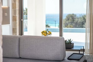 Un salón moderno con un sofá gris, una mesita con una planta y vistas al mar a través de amplios ventanales.