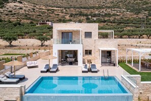Una casa moderna de dos pisos con piscina, mobiliario exterior y vistas a olivos.