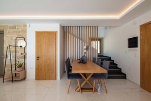 A modern dining area with a wooden table and chairs, a staircase, and a stone wall.