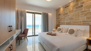 A modern hotel room with a large bed, a desk, and a chair. There is a view of the ocean through the window.