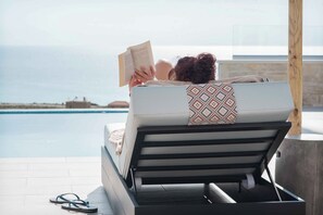 En person som kopplar av på en solstol vid en pool med utsikt över havet.