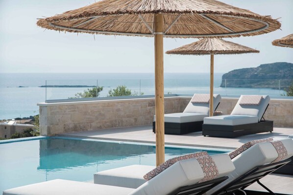 A poolside area with lounge chairs and thatched umbrellas, overlooking a body of water.