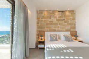 A bedroom with a stone wall, a bed with two pillows, a nightstand, and a view of the ocean.