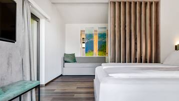 Una habitación de hotel moderna con una cama grande, un banco, un sofá y vistas a un paisaje montañoso a través de una ventana.