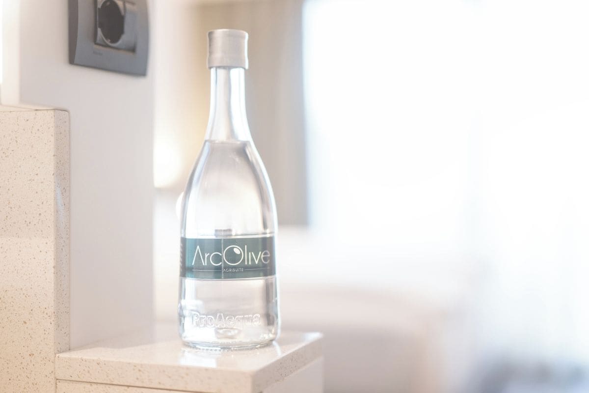 A clear bottle of Marc Olive water on a white surface.