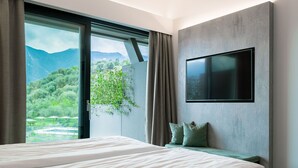 Une chambre d’hôtel moderne avec un grand lit, un téléviseur fixé au mur et une vue sur les montagnes par la fenêtre.