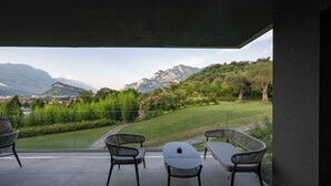 Un balcon avec une table et des chaises, donnant sur un paysage verdoyant et des montagnes.