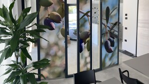 Une chambre moderne dotée d’une grande porte-fenêtre coulissante ornée d’une fresque représentant un manguier décoratif, d’une table à manger avec des chaises et d’une plante en pot.