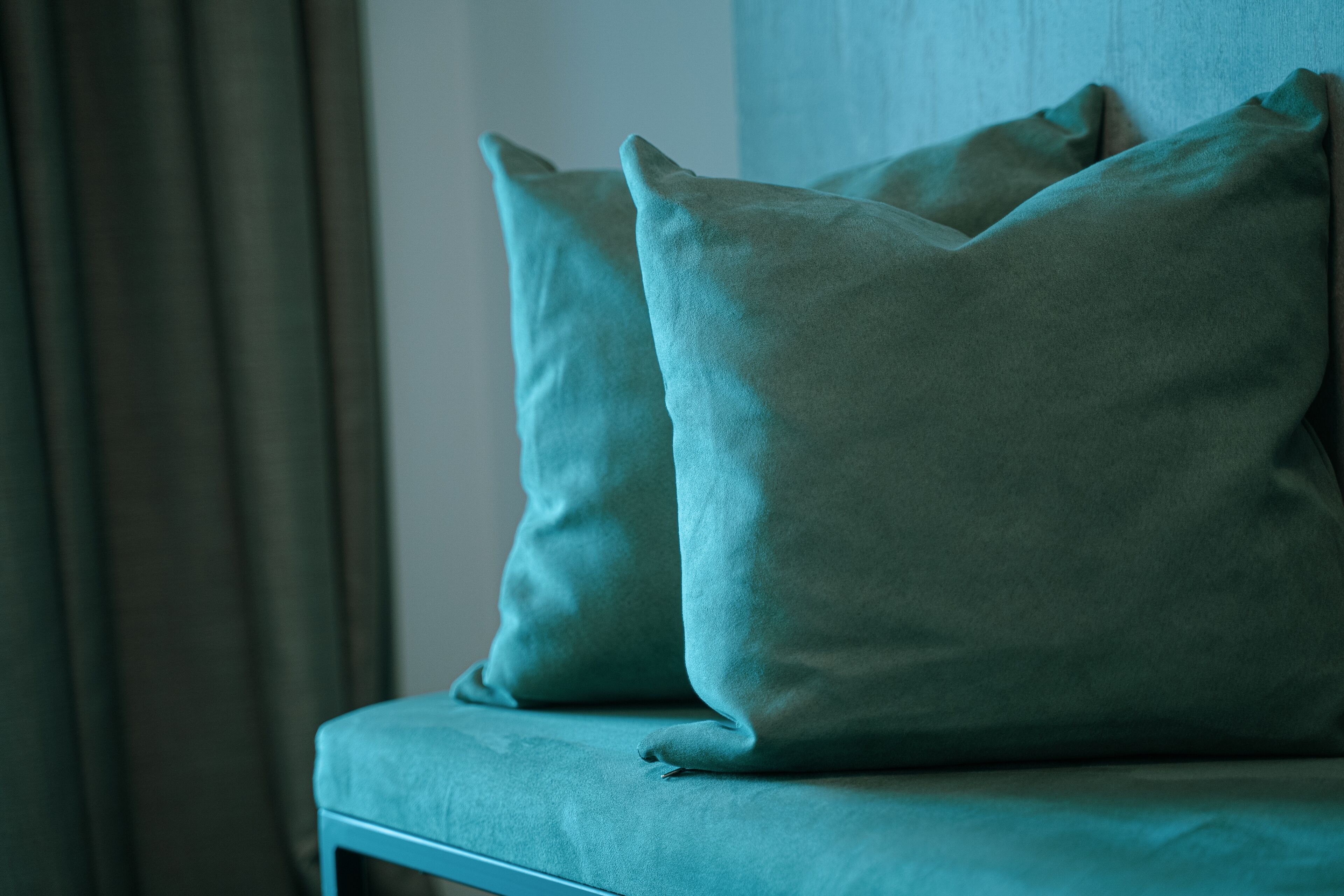 A teal sofa with two cushions against a wall.