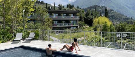 Una piscina con agua cristalina, rodeada por una valla metálica, con vistas a un paisaje montañoso y un edificio al fondo.