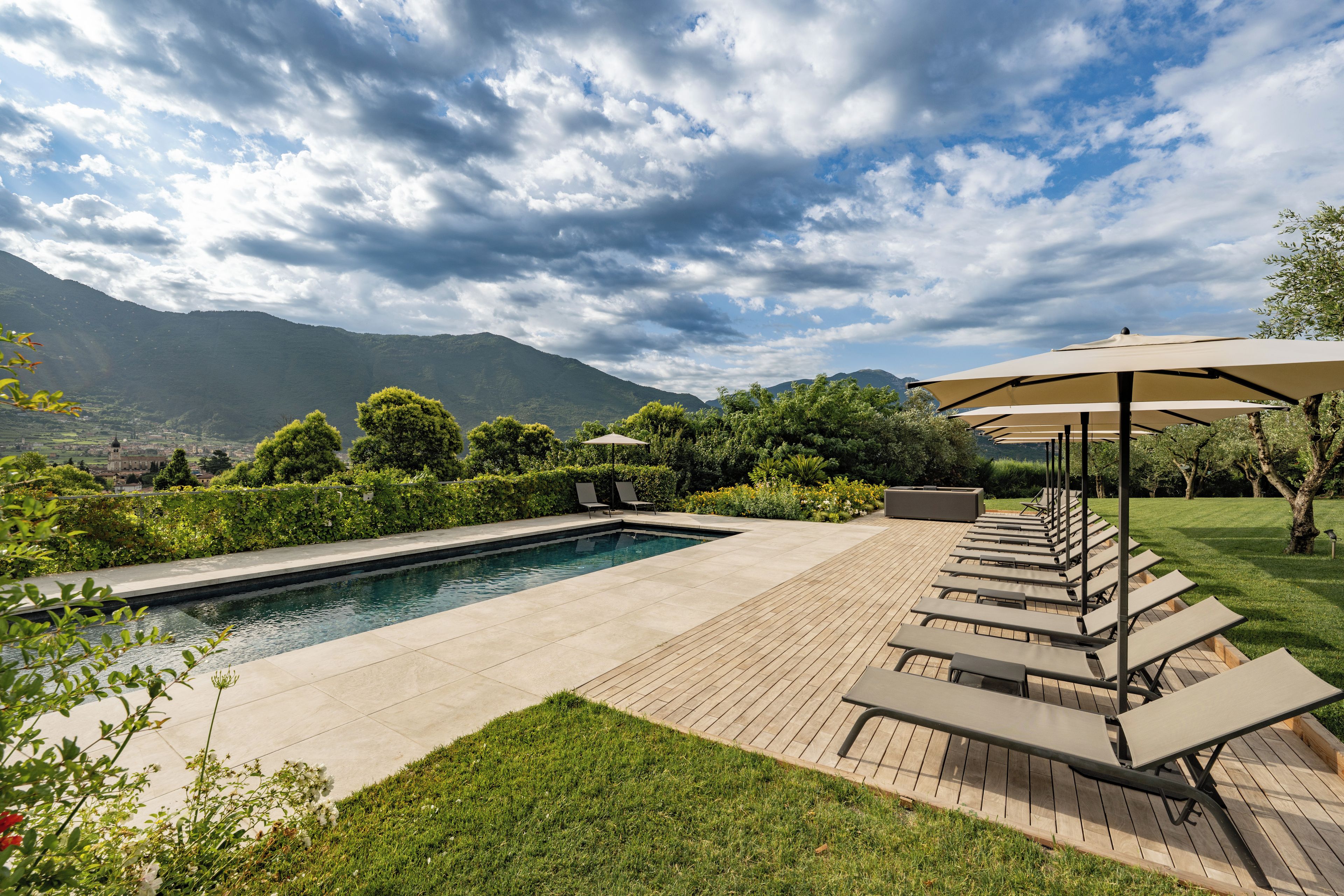 A swimming pool with lounge chairs and umbrellas, surrounded by greenery and mountains in the background.