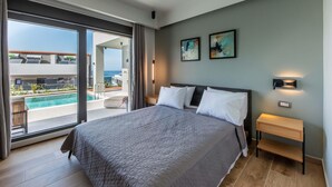 A modern bedroom with a large bed, a nightstand, and a view of a swimming pool and building.