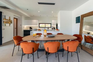 A modern dining area with a round wooden table surrounded by orange chairs, a vase, and a bowl. - Lusol Seafront Villas-Free* Heated Pools, 100m Sea (Chania)