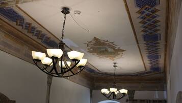 Un candelabro con múltiples lámparas colgando del techo en una habitación con adornos murales estampados y una ventana.